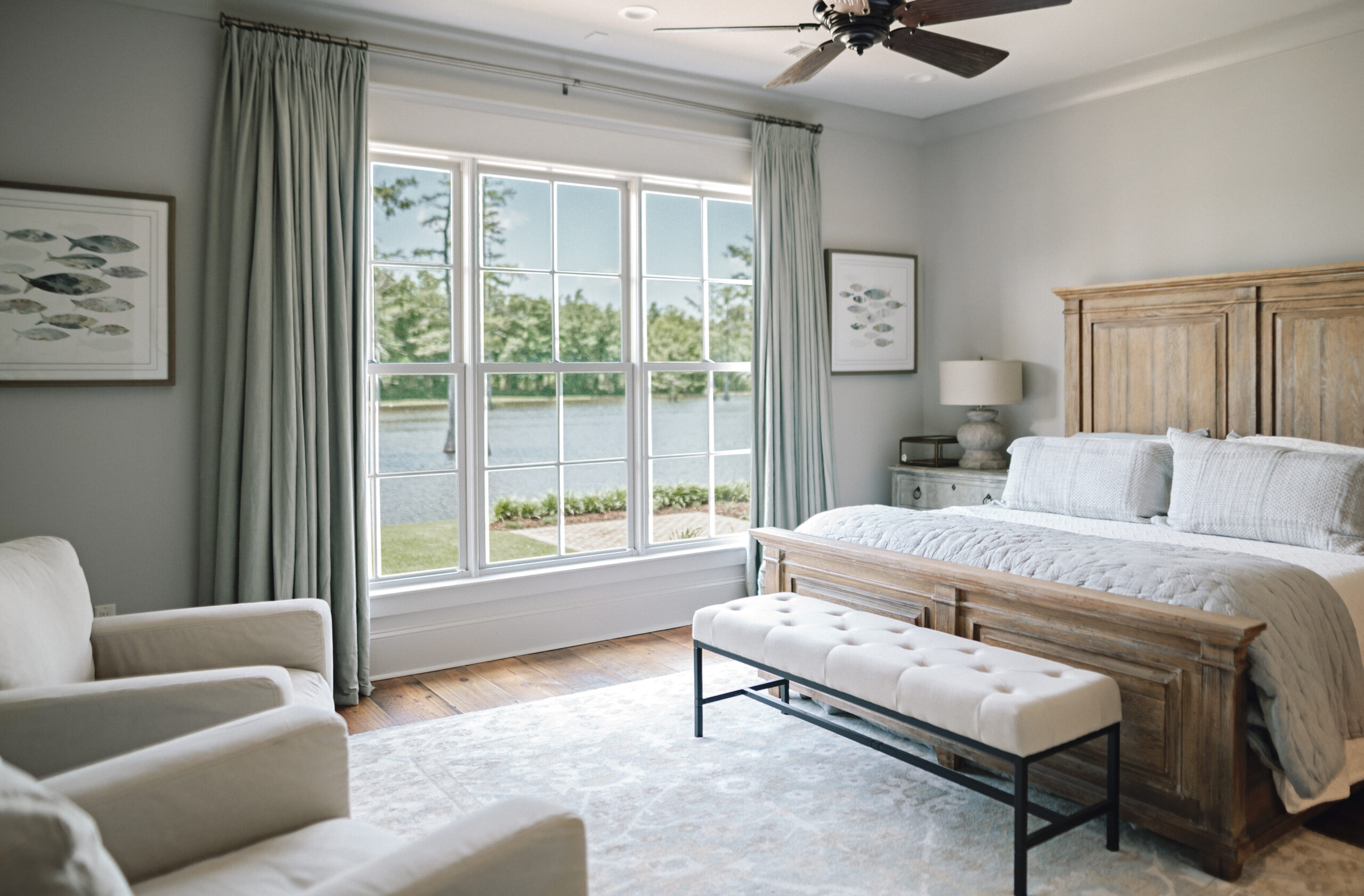 bedroom with brown wooden bed frame, grey and white bedding, white bench, beige accent chairs, and light blue green accent colors